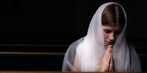 A young modest girl with a handkerchief on her head is sitting in church and praying. The concept of religion, prayer, worship.