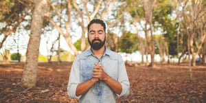 A man praying in a sunlit forest. 