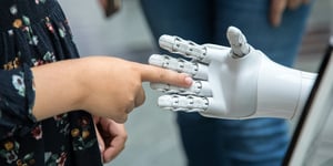 A little girl touching a robotic hand. 