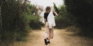 Woman walking down a road with her jack thrown over her shoulder. 