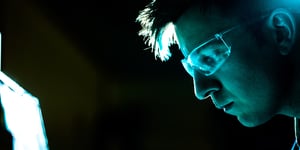 Man with safety goggles with his face illuminated by a blue light.