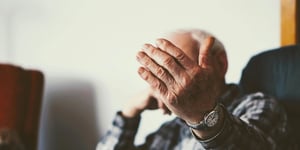 An old man holding his hand up in front of his face.