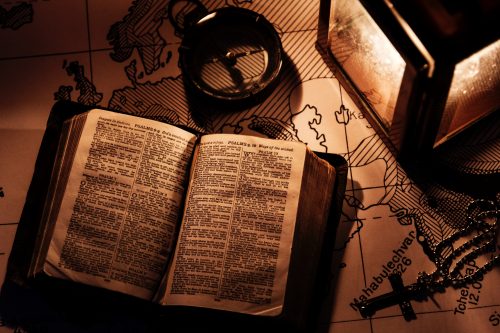 bible, compass, rosary and lantern on a map