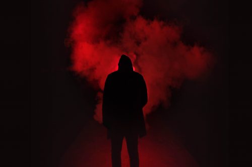 man in hood silhouetted against red smoke