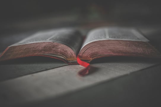 A half open bible on a table with a red ribbon book market.