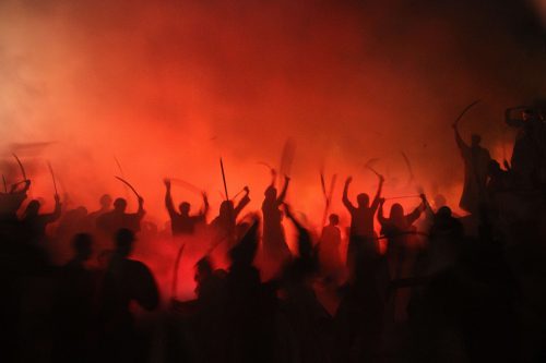 men brandishing weapons in lurid firelight