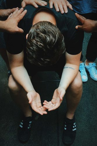 man with bowed head with many hands laid upon him