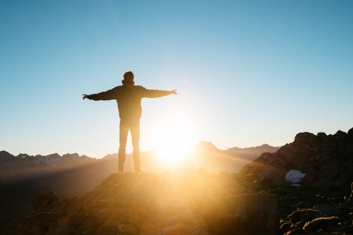 man stands with outstretched arms facing rising sun