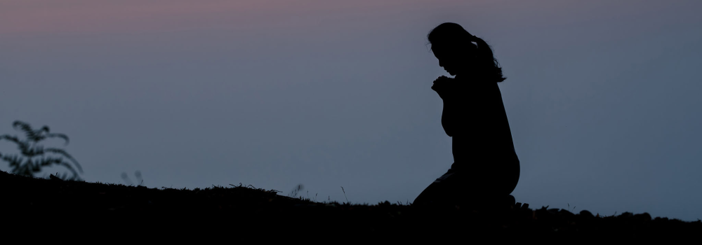 A woman praying at dusk/dawn.